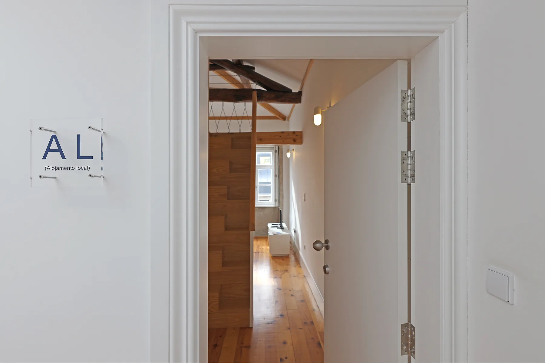 A doorway opens onto a narrow hallway with wood flooring and a staircase.