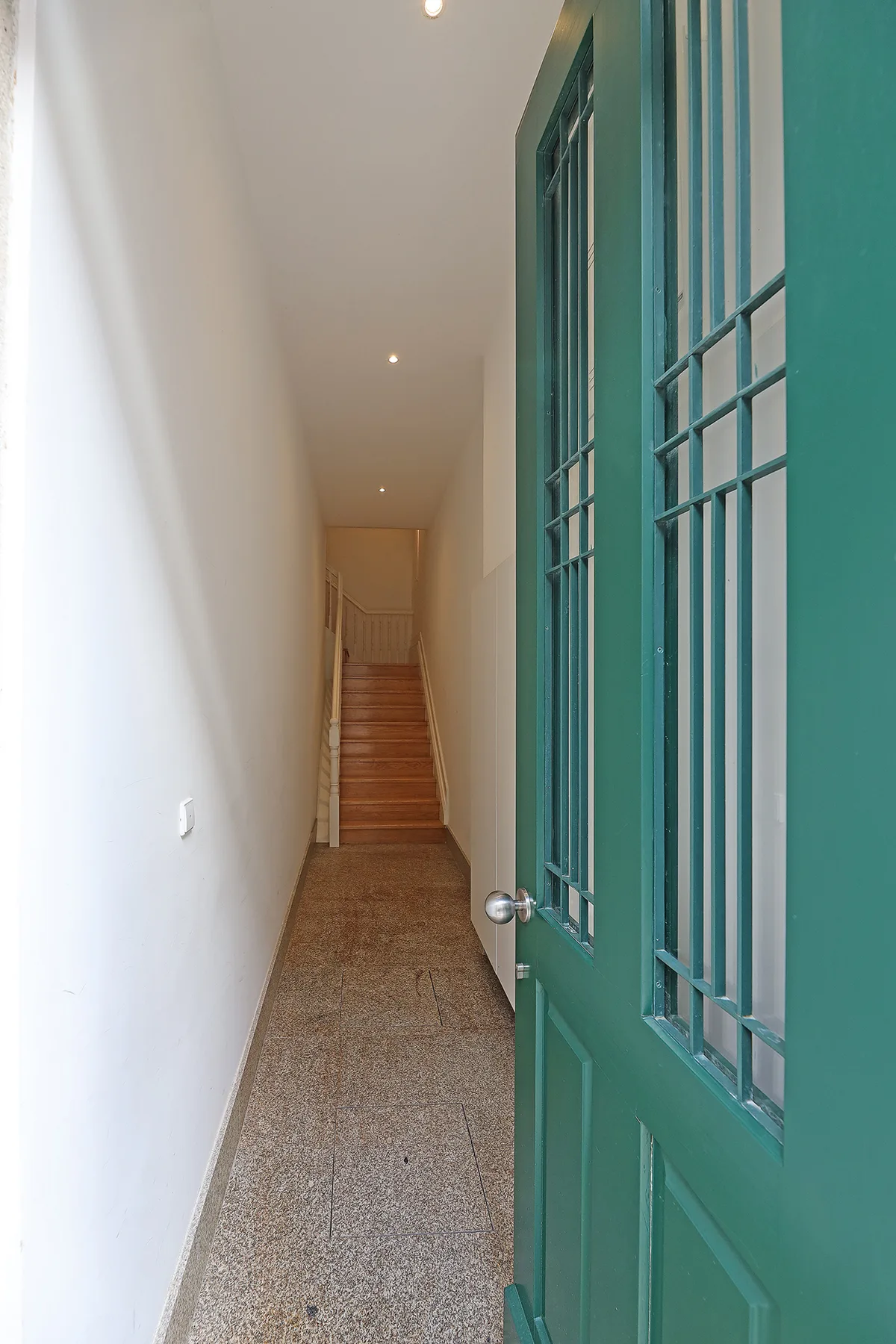 A narrow hallway with a staircase at the far end and an open green door.