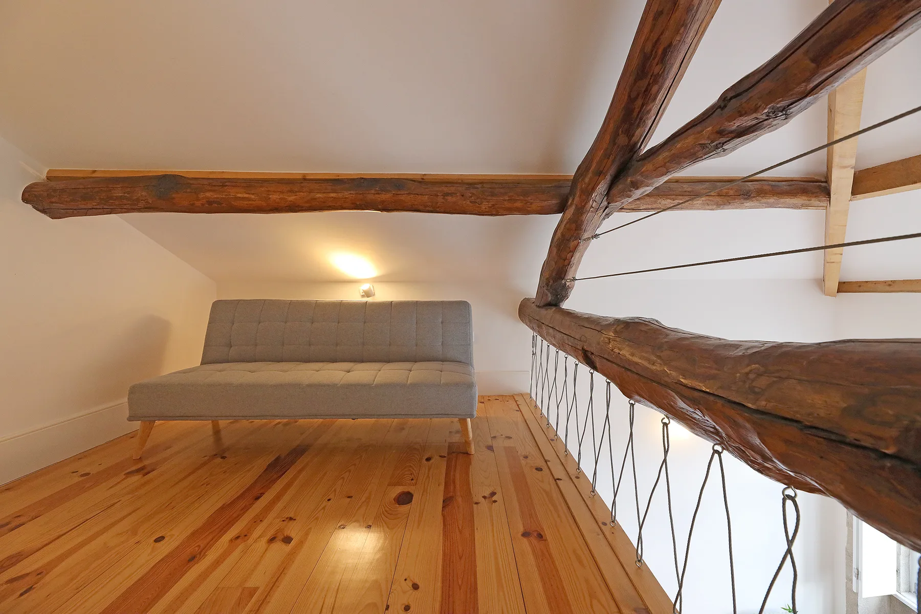 Una zona de estar tipo loft con un sofá gris bajo vigas de madera.