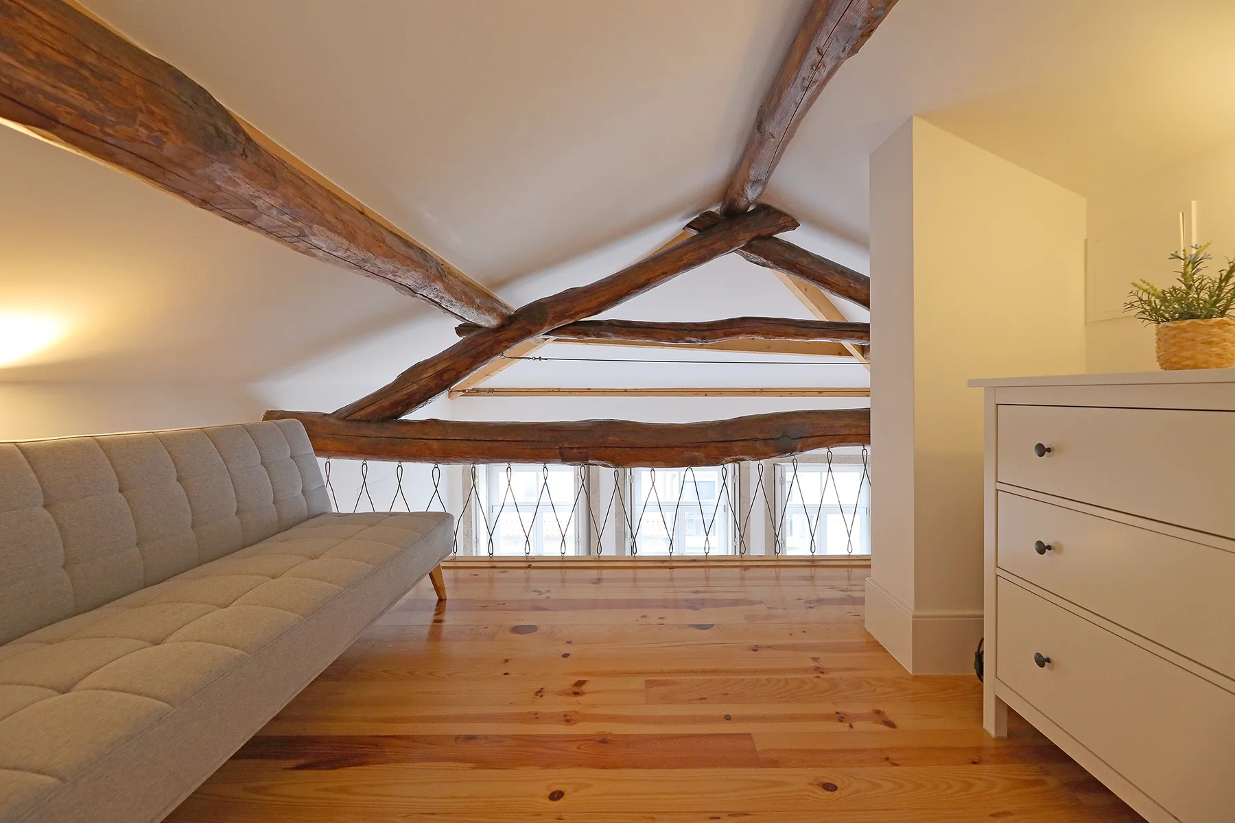 Una sala tipo loft con un sofá gris bajo vigas de madera a la vista.