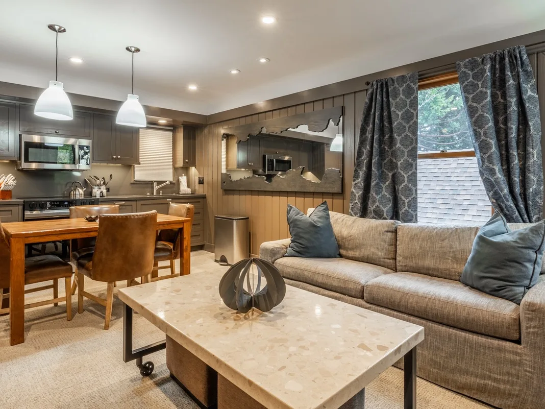 Una sala de estar con sofá y mesa de centro junto a una cocina abierta y comedor.