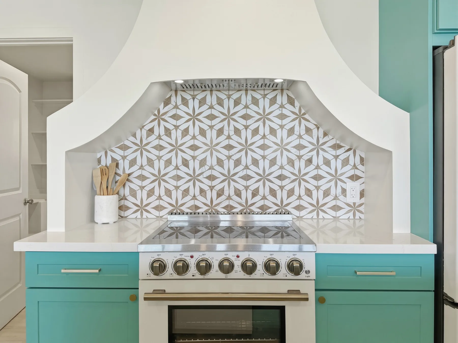A turquoise kitchen centers on a stainless-steel range beneath a patterned tile backsplash.