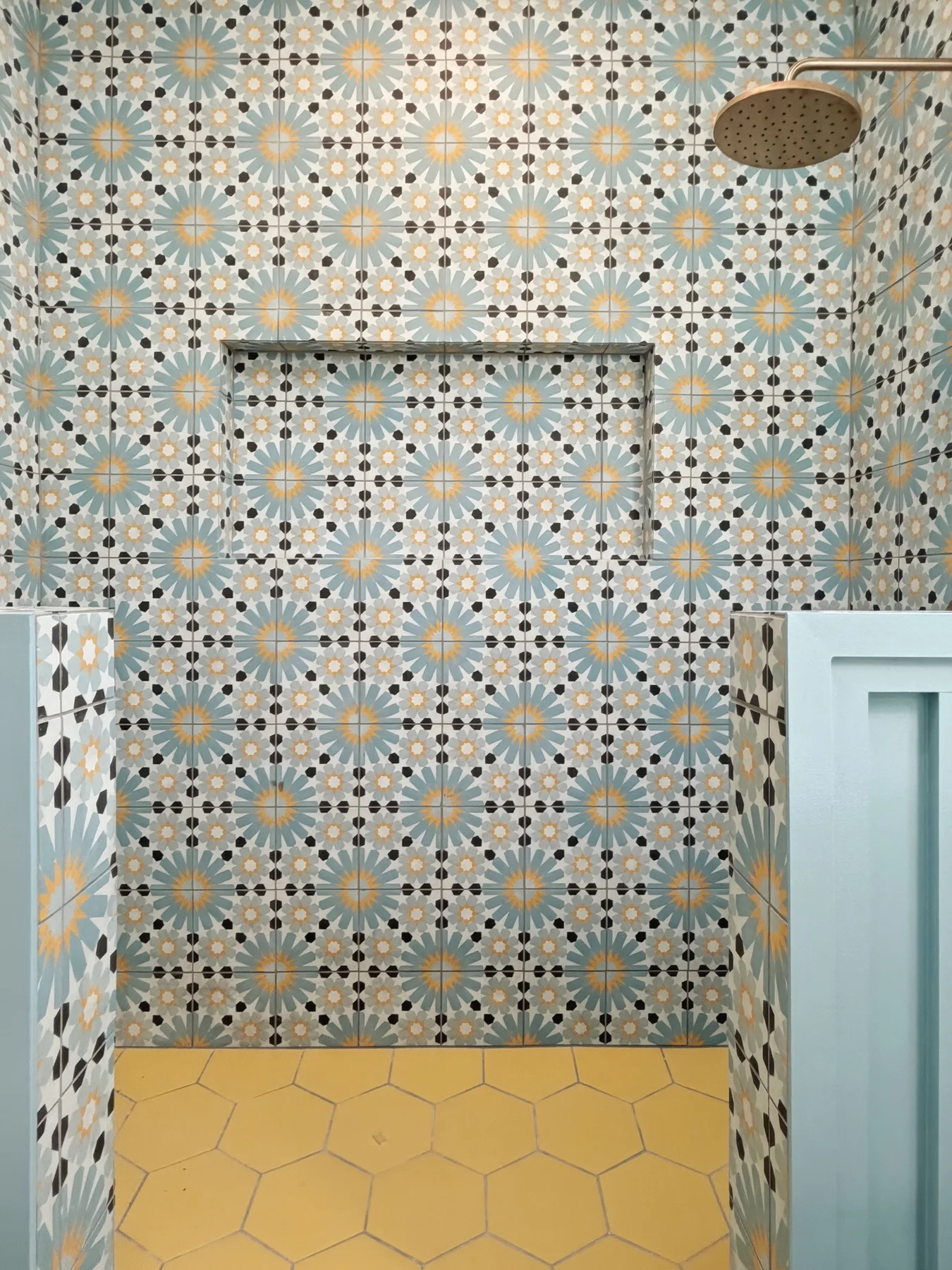 A tiled shower area with patterned walls and a yellow floor.