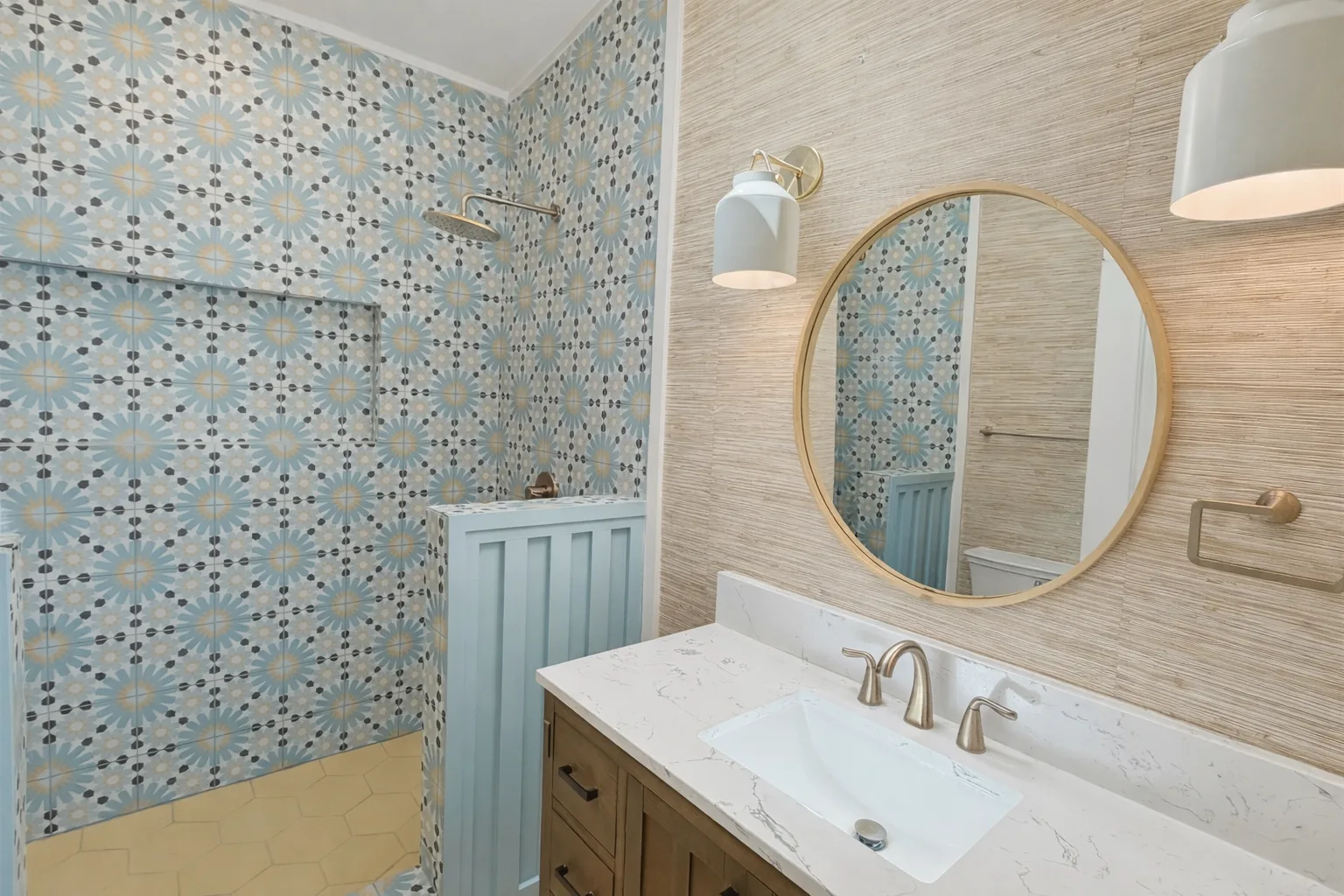 A bathroom with patterned tile, a glass shower, and a sink beneath a round mirror.