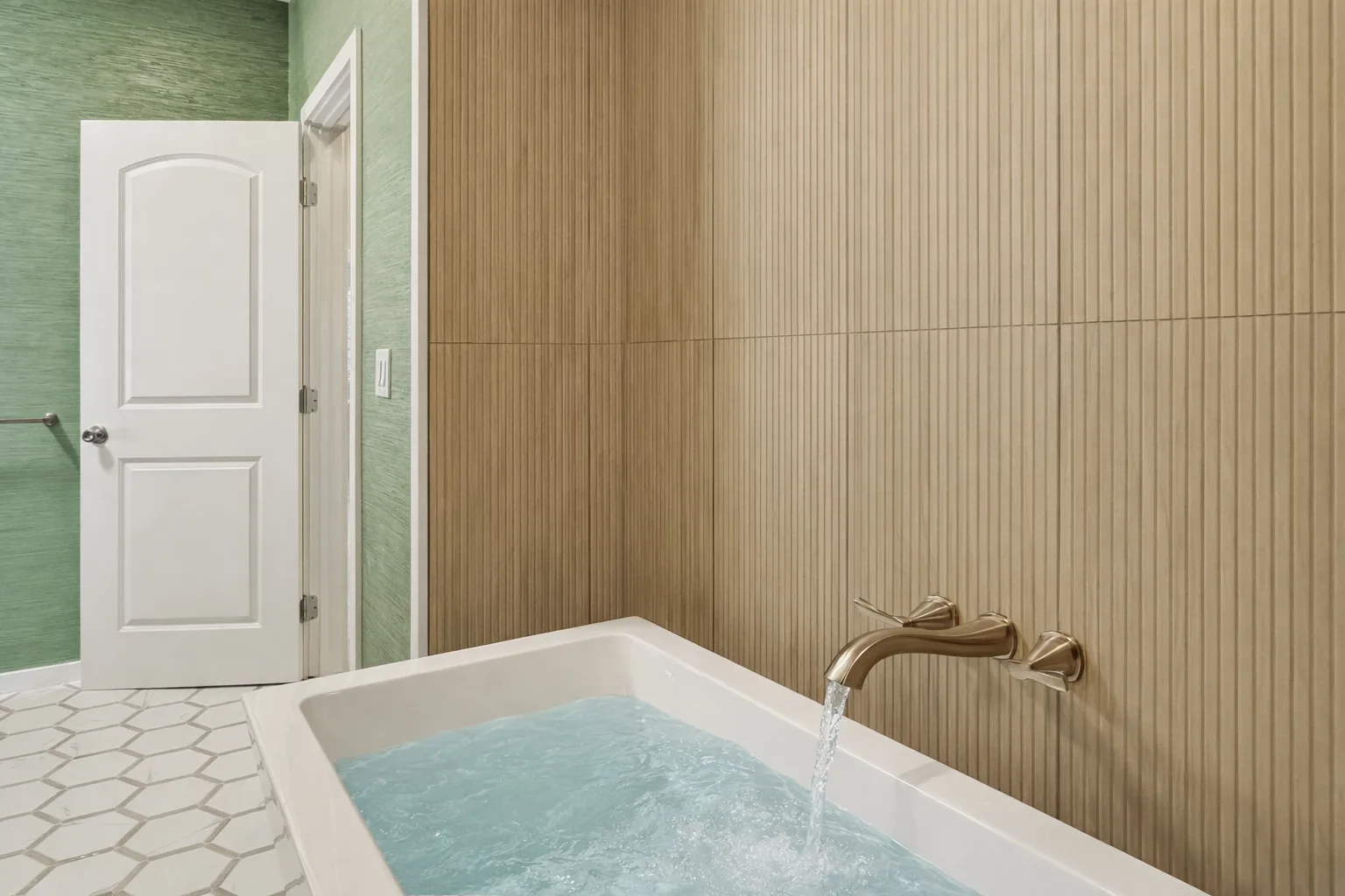 A bathtub filled with water sits beside a white door in a tiled bathroom.