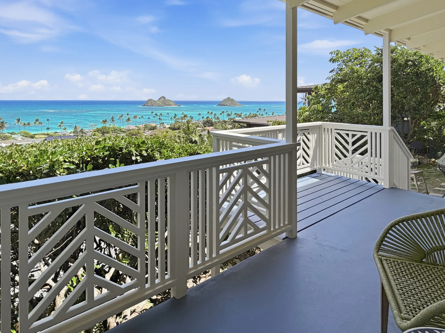 A balcony overlooks a turquoise ocean, with white railings and a leafy shoreline.