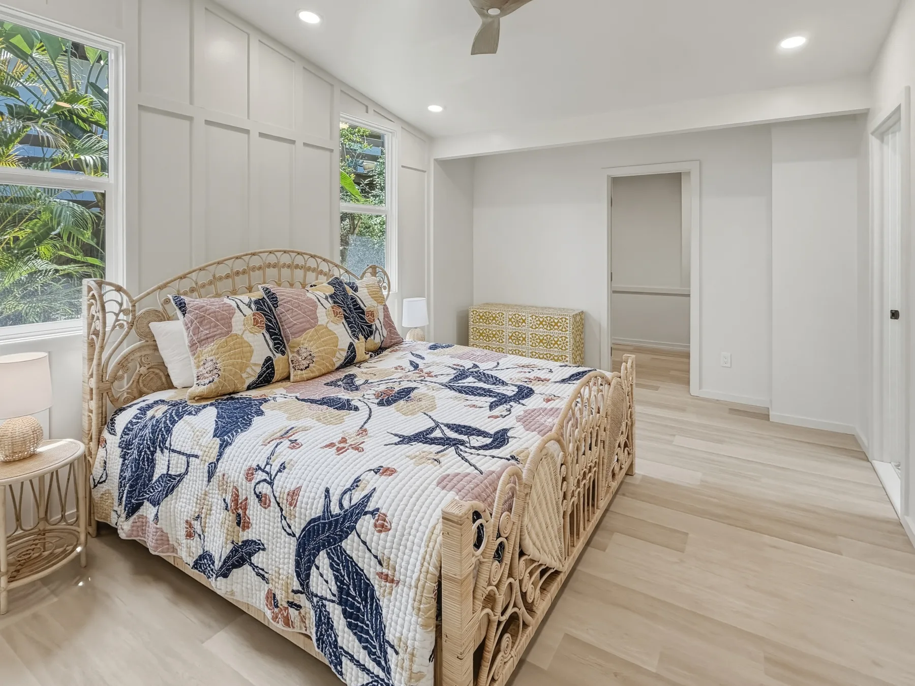 A bright bedroom with a patterned bed and windows overlooking greenery.