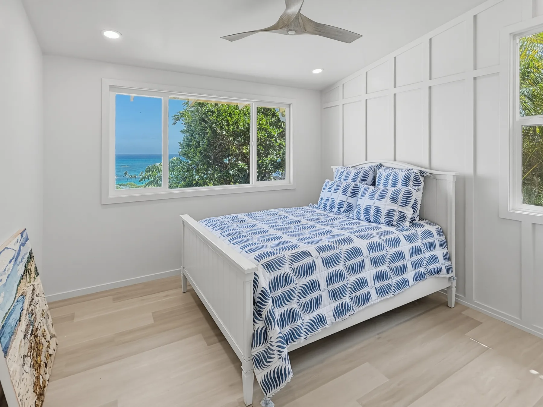 A bright bedroom with a bed beside a wide window overlooking the sea.