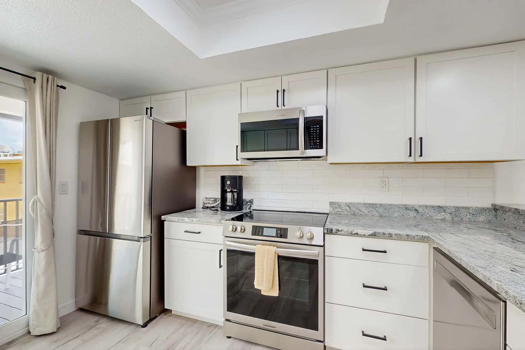 A bright kitchen with white cabinets, stainless steel appliances, and stone countertops.