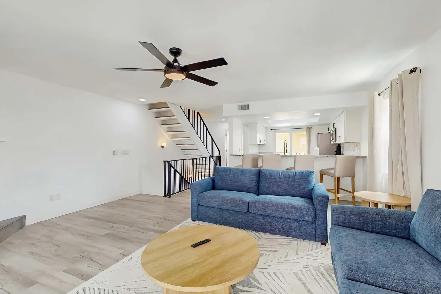 Open-plan living area with blue seating, a coffee table, and a kitchen beyond.