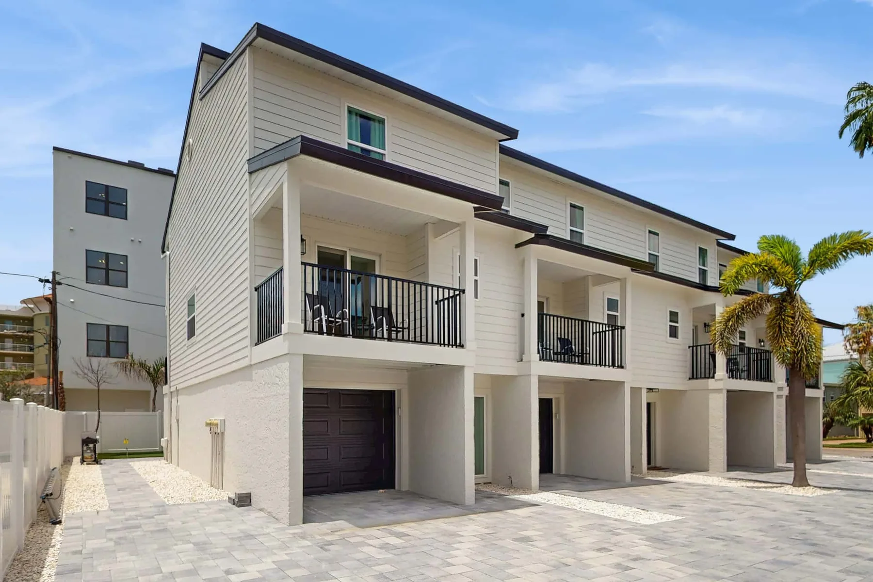 A row of modern townhouses with balconies, garage doors, and a paved driveway.