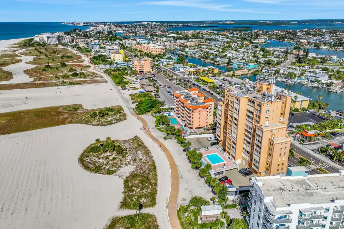 Aerial view of coastal buildings beside a sandy shoreline and water.