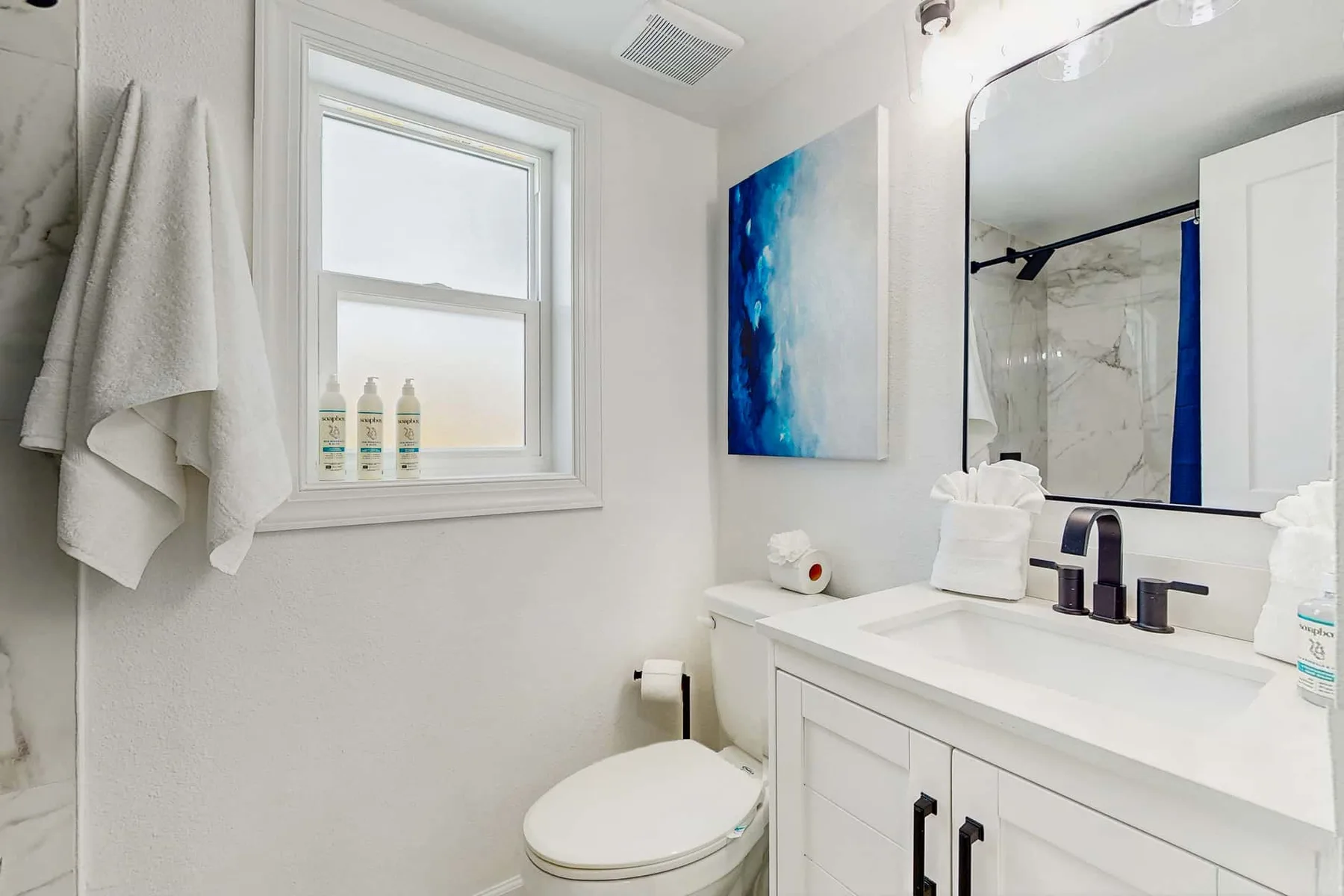 A bright bathroom with a white vanity, mirror, and window.