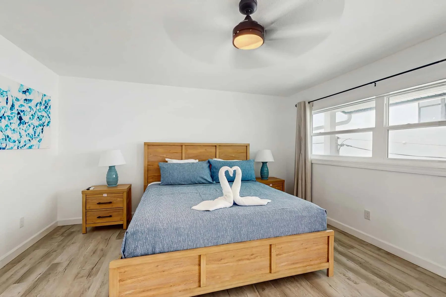 A bright bedroom with a wooden bed, blue bedding, and a large window.