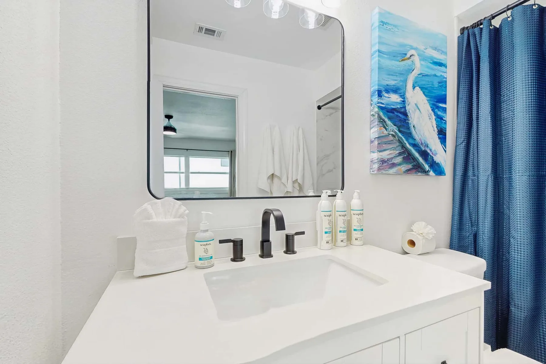 A bright bathroom vanity with a sink, large mirror, and blue shower curtain.