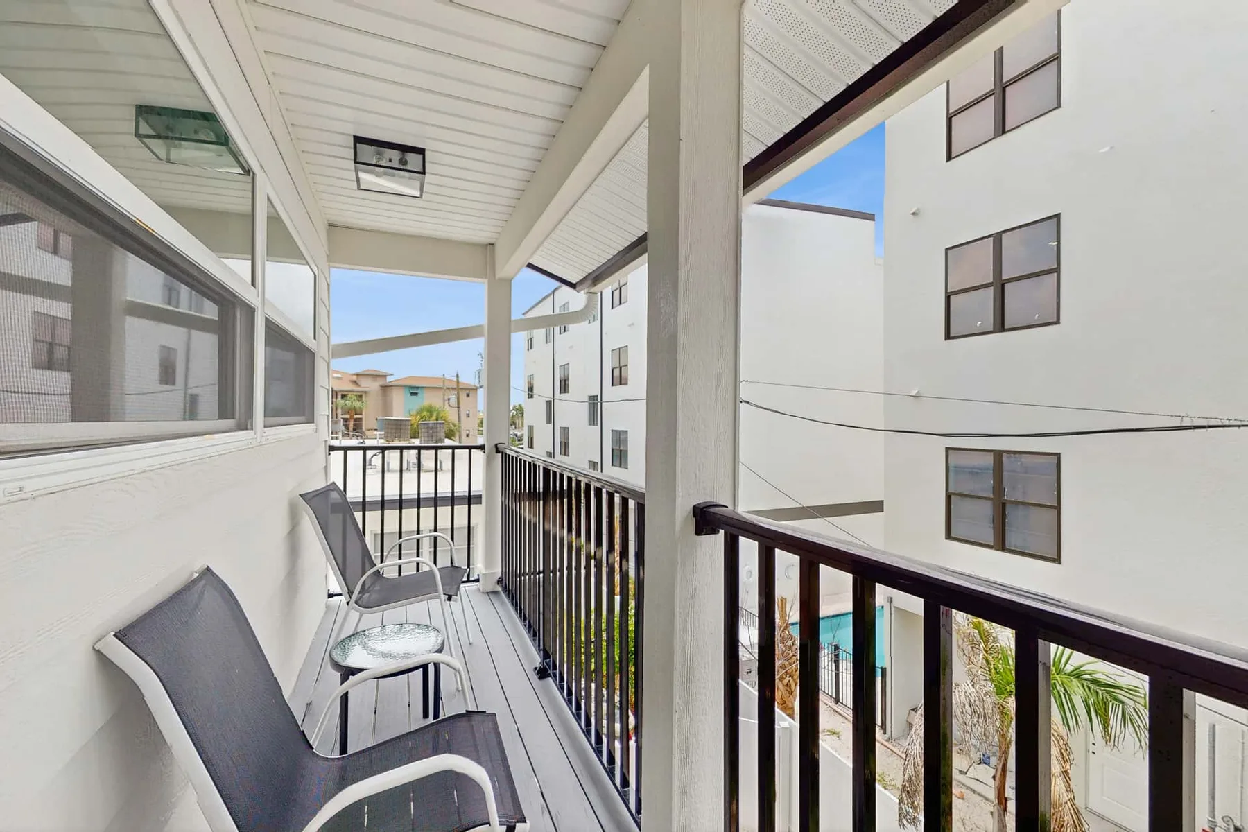 A narrow outdoor balcony with seating overlooks nearby apartment buildings.