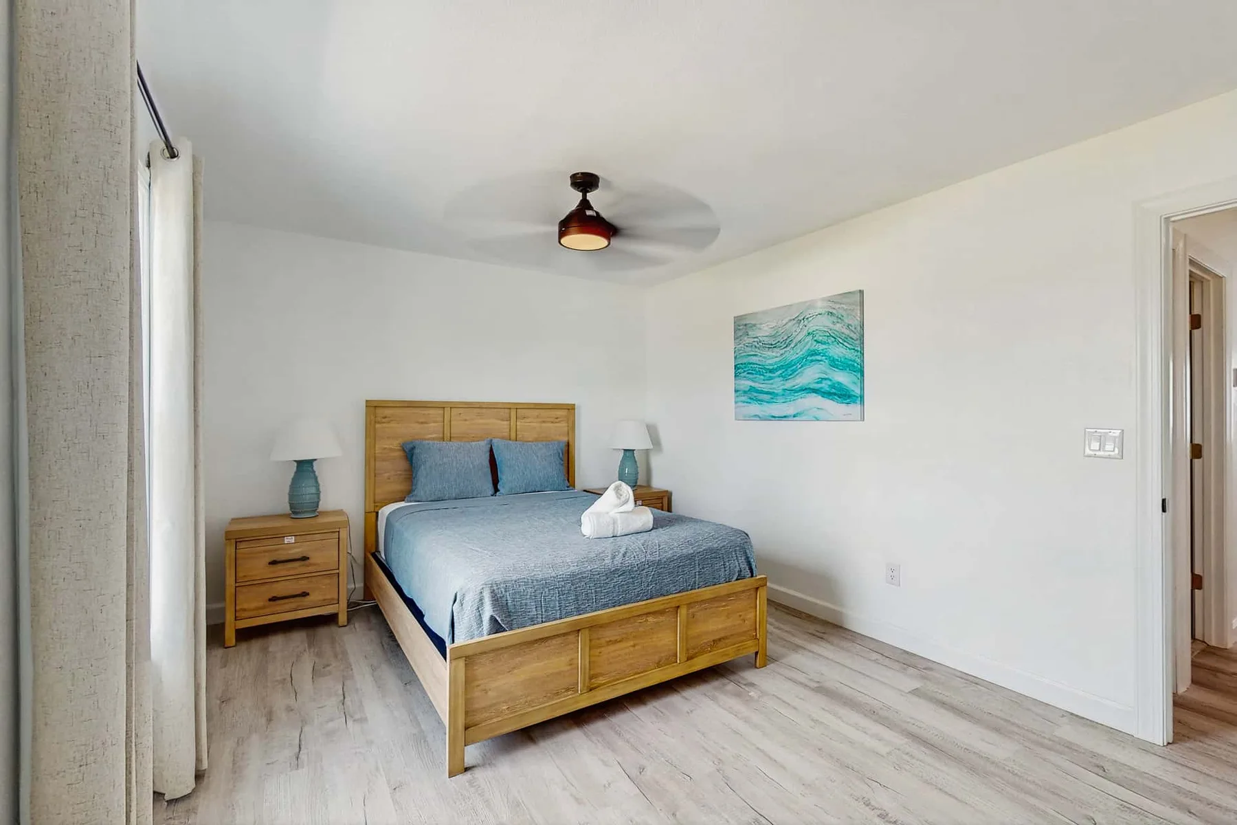 A bright bedroom with a wooden bed, blue bedding, and a ceiling fan.