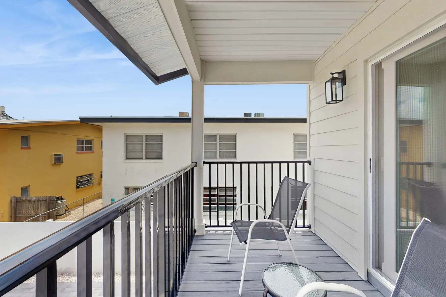 A covered balcony with outdoor seating and a railing overlooks nearby buildings.