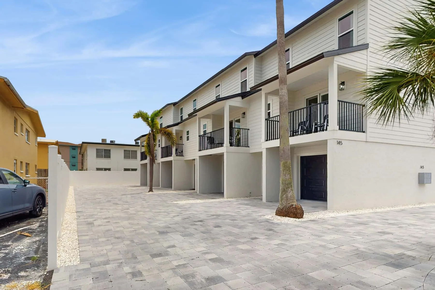 A paved courtyard runs alongside a row of white buildings with balconies.