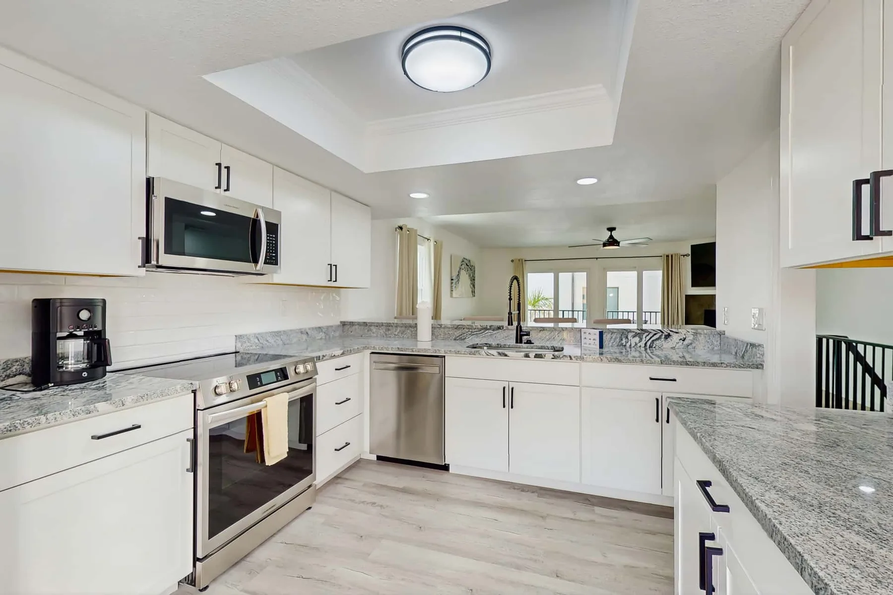A bright kitchen with white cabinets, stone countertops, and stainless steel appliances.