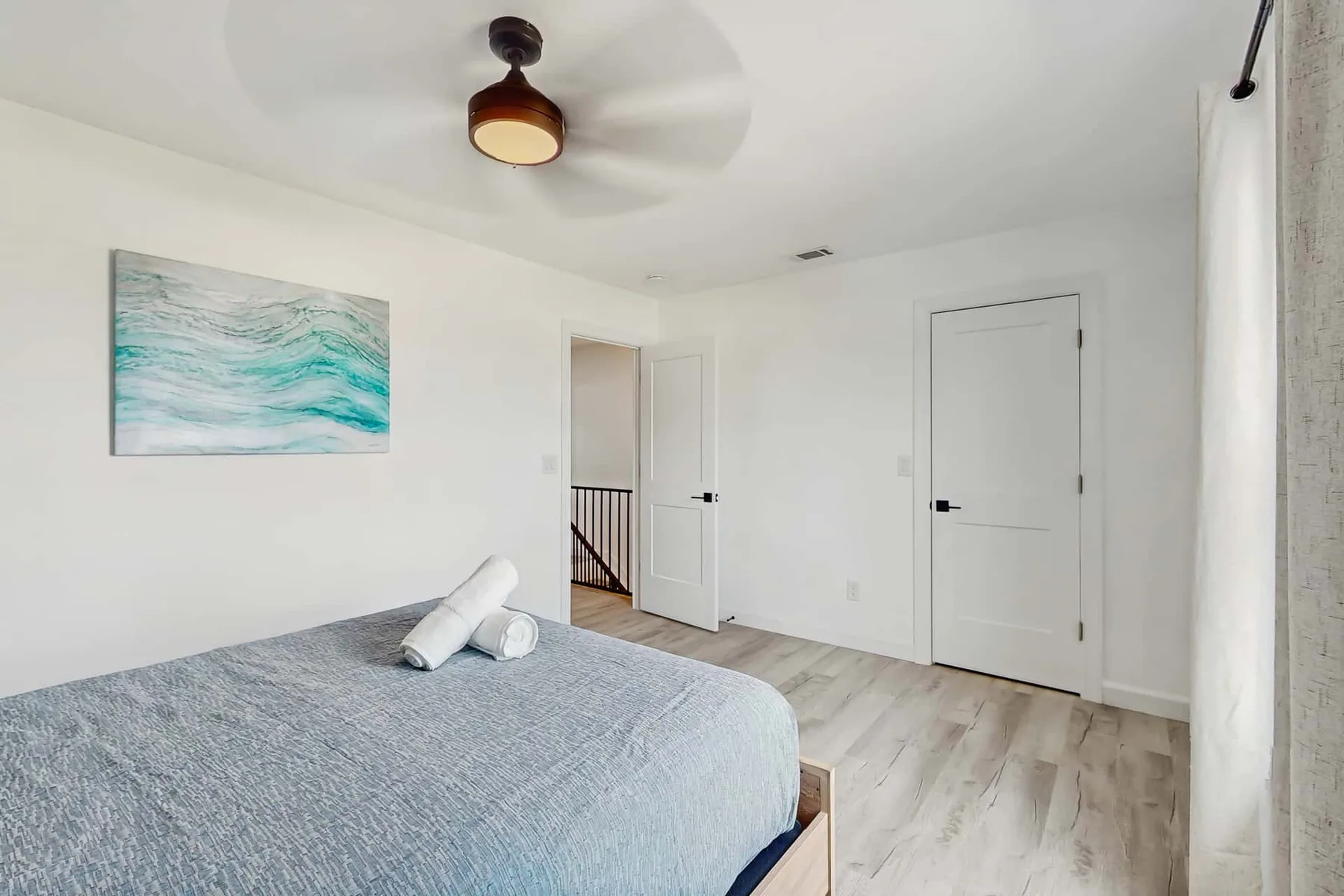 A bedroom with a bed, wall art, and a ceiling fan.