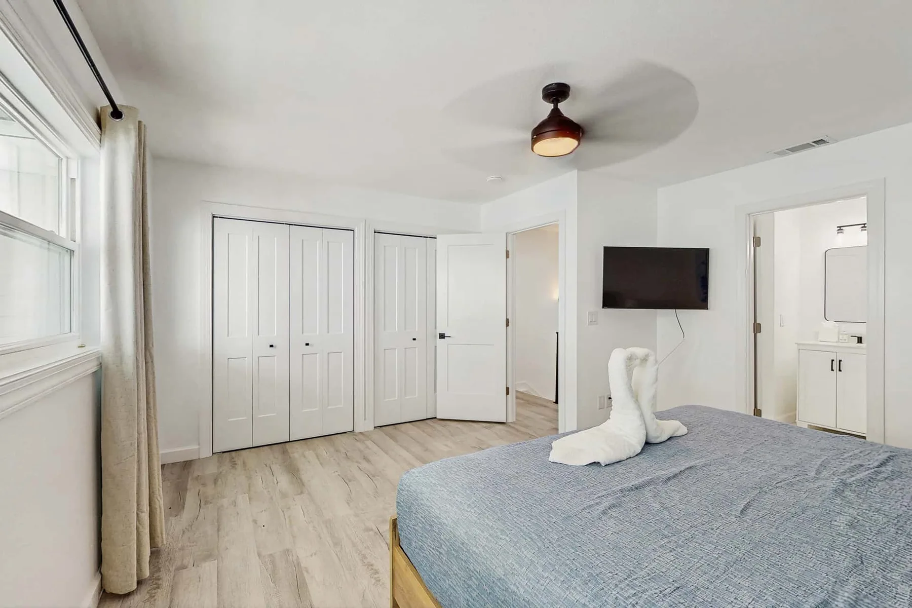 A bright bedroom with a bed, white closet doors, and a wall-mounted television.