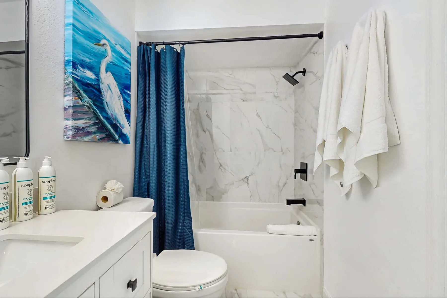 A bathroom with a bathtub, blue shower curtain, and white towels.