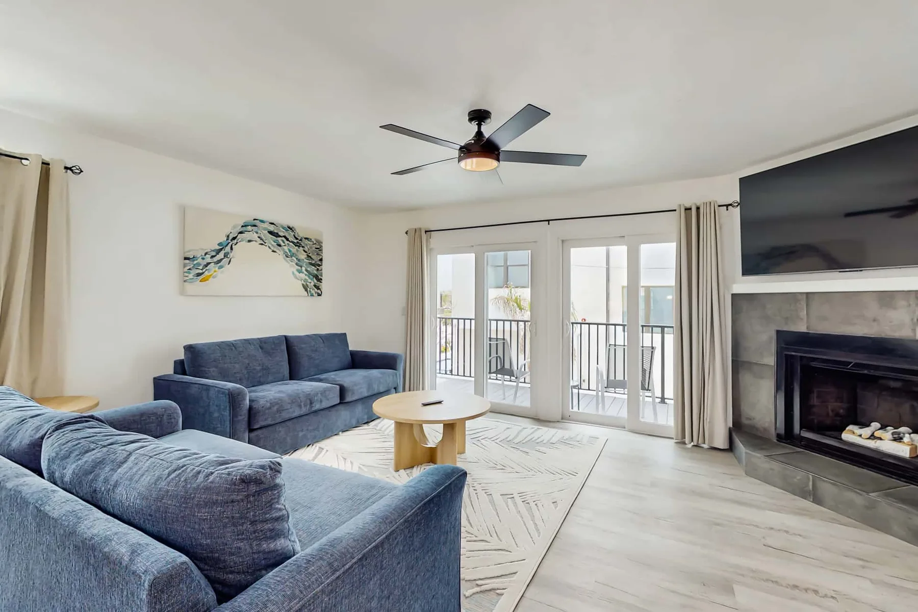 A bright living room with blue seating, balcony doors, and a fireplace.