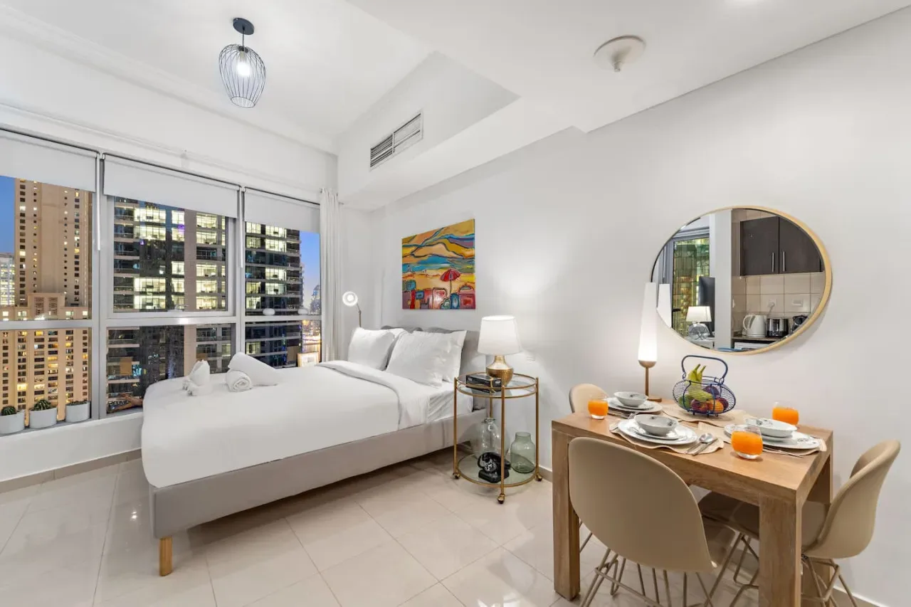 Un dormitorio luminoso con una cama junto a grandes ventanas y una mesa pequeña.