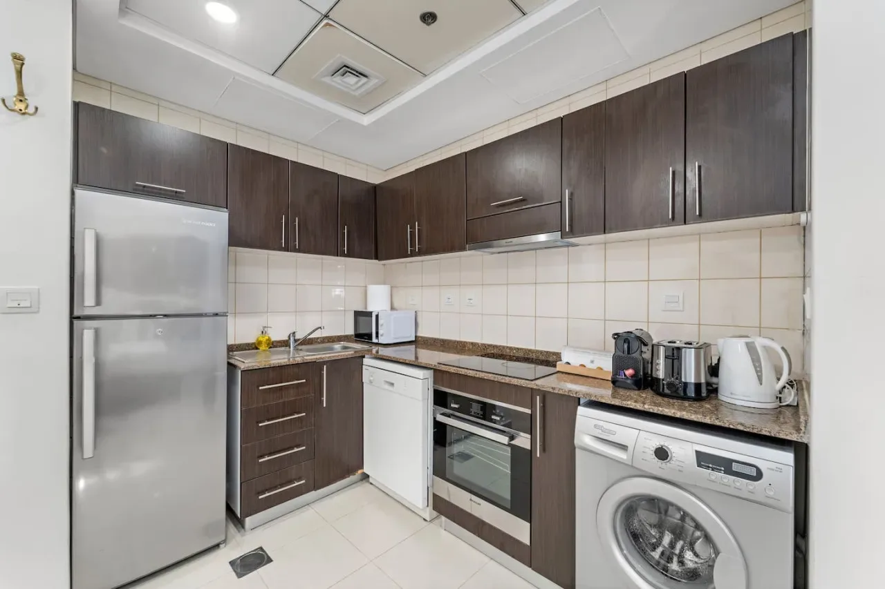 Una cocina compacta con armarios oscuros, un refrigerador y electrodomésticos integrados.