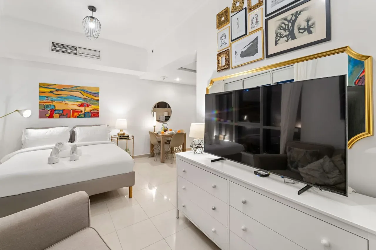 Un dormitorio luminoso con una cama, un televisor grande y cuadros enmarcados.