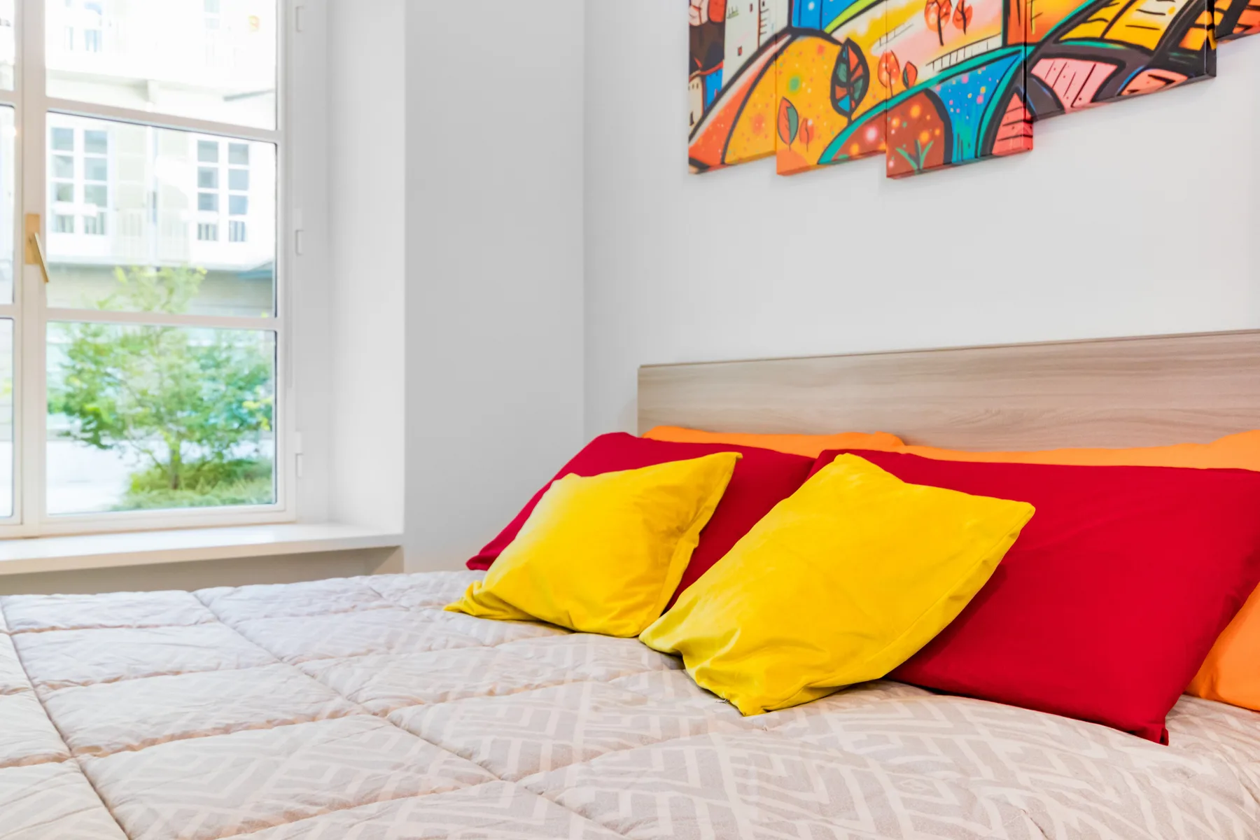 Un dormitorio con una cama, almohadas coloridas y una obra de arte sobre el cabecero.
