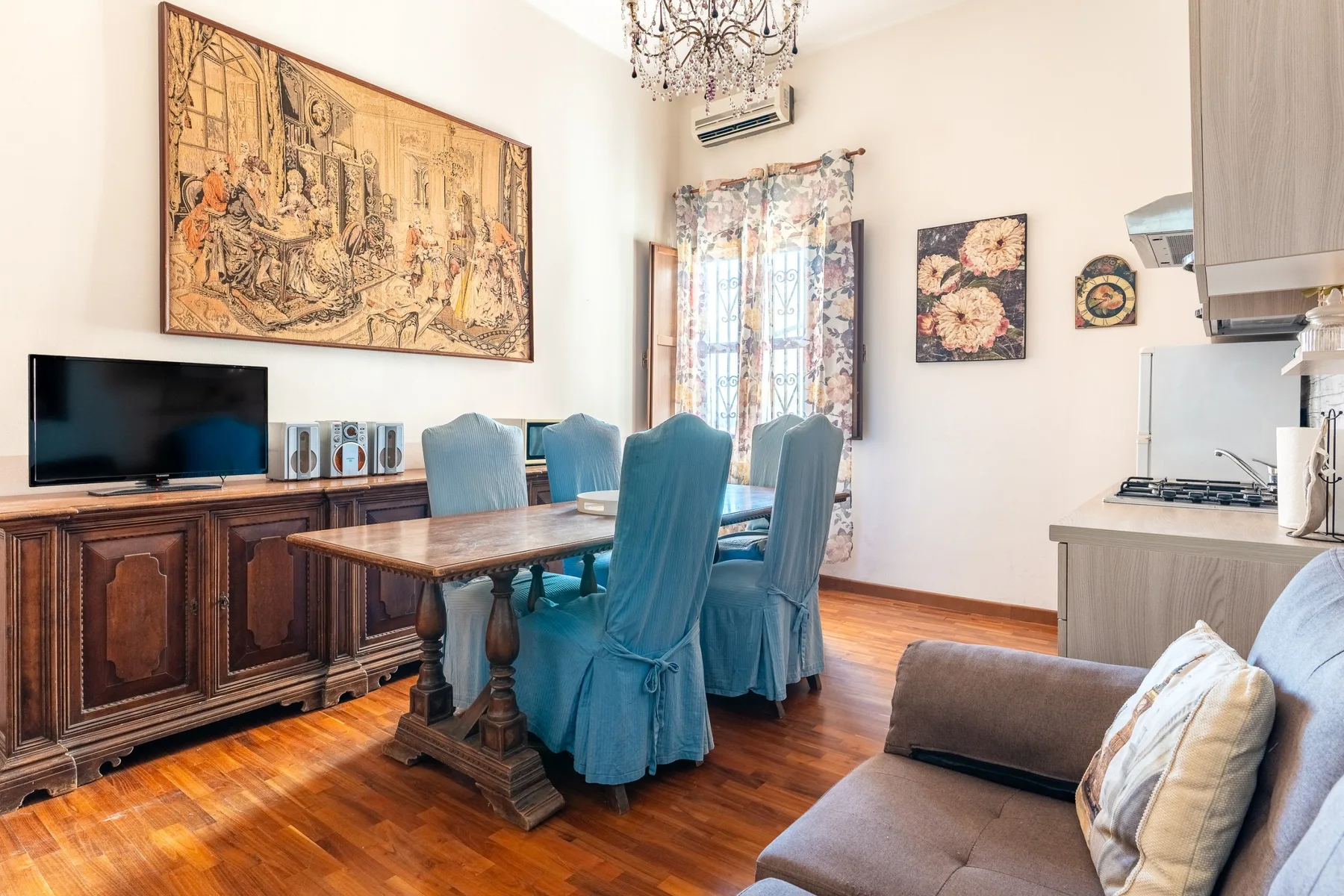 Una zona de comedor y estar con una mesa de madera, asientos azules y un televisor.