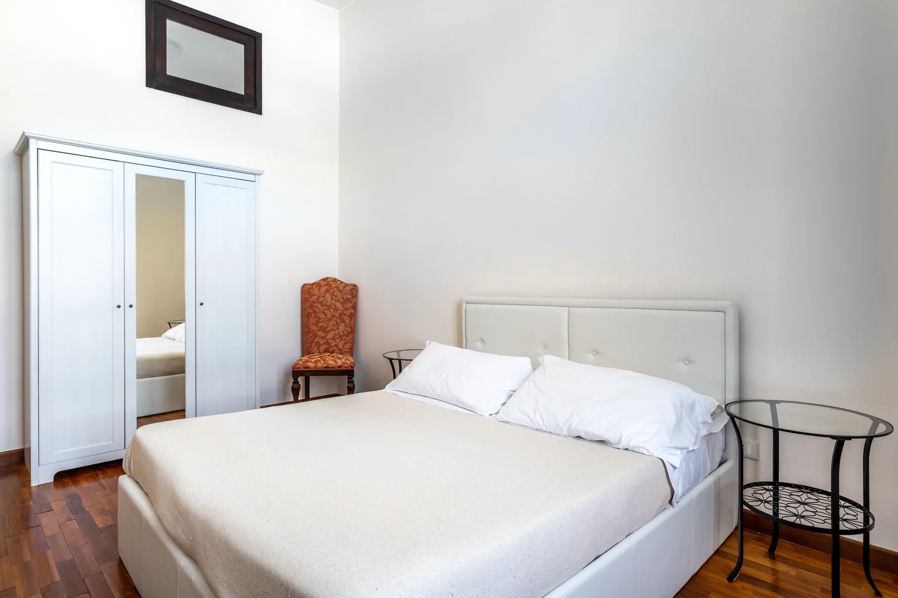 Un dormitorio luminoso con una cama, un armario con espejo y suelo de madera.