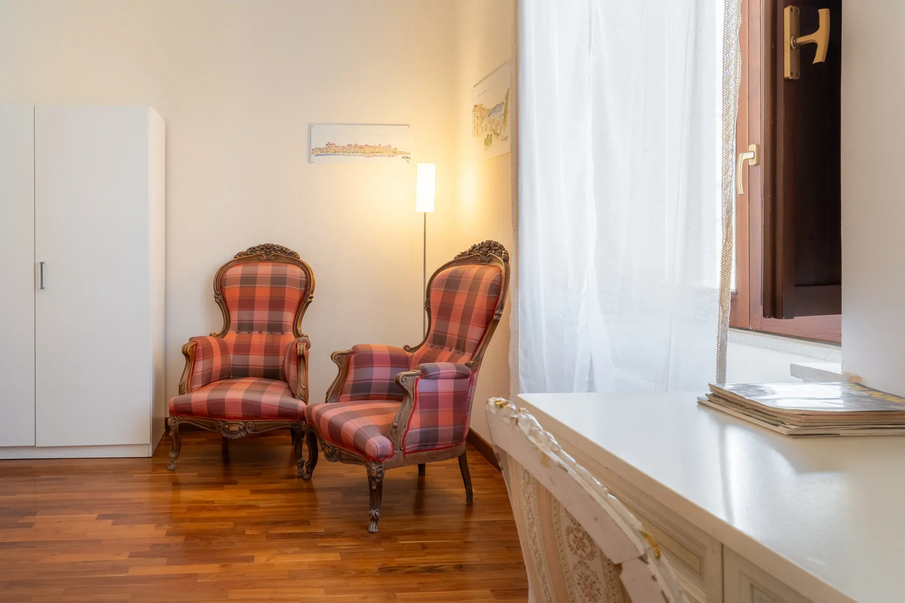 Una habitación luminosa con dos asientos tapizados a cuadros junto a una ventana con cortina.
