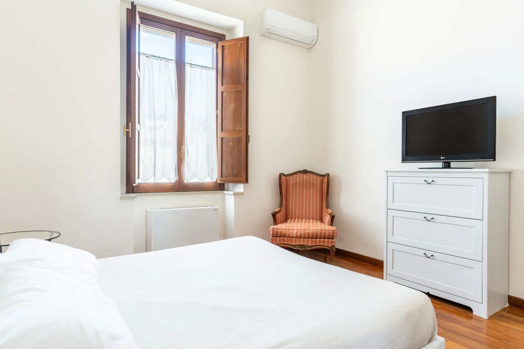 Un dormitorio con una cama, un sillón y un televisor sobre una cómoda.