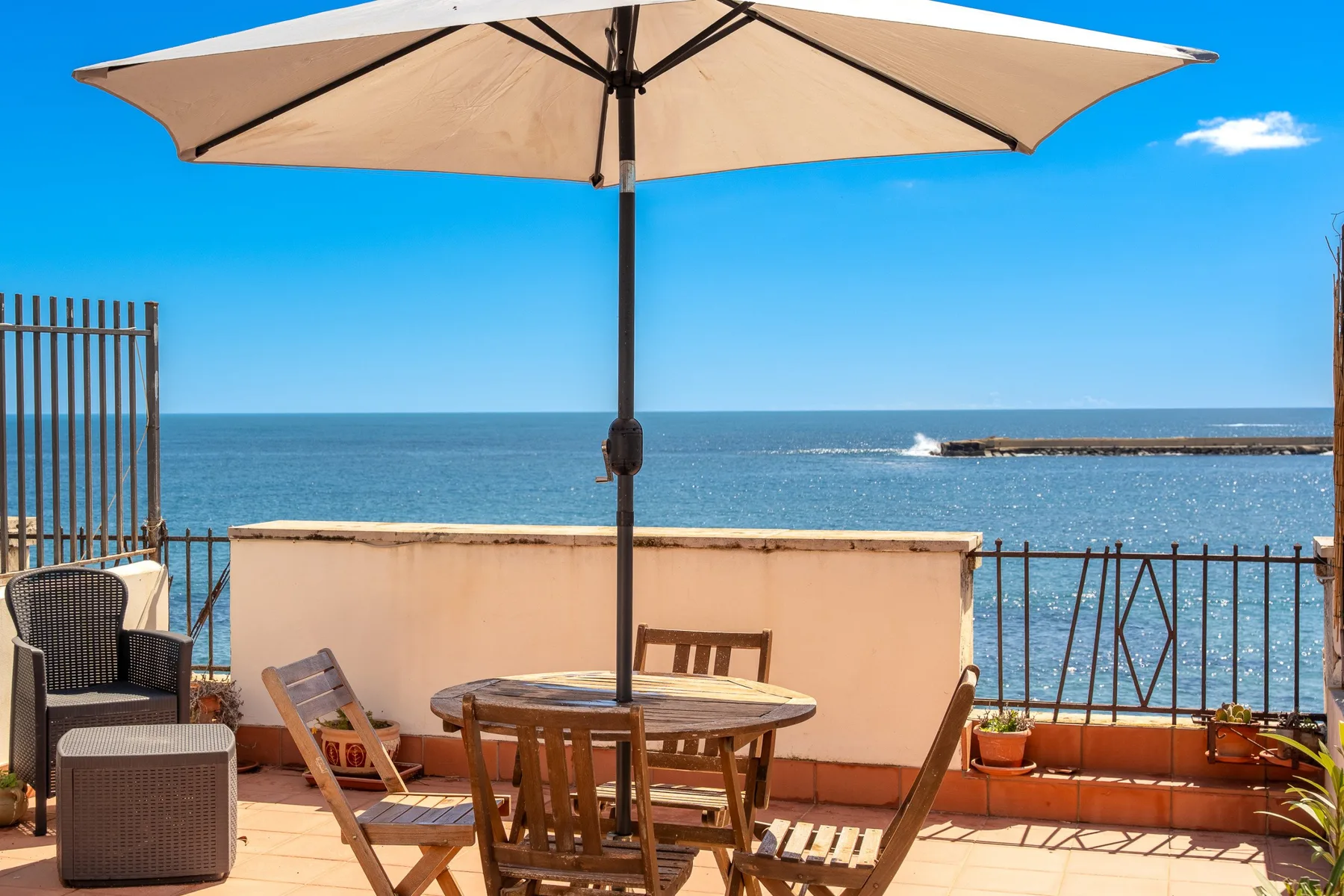Una terraza junto al mar con mesa y sombrilla, frente al agua.