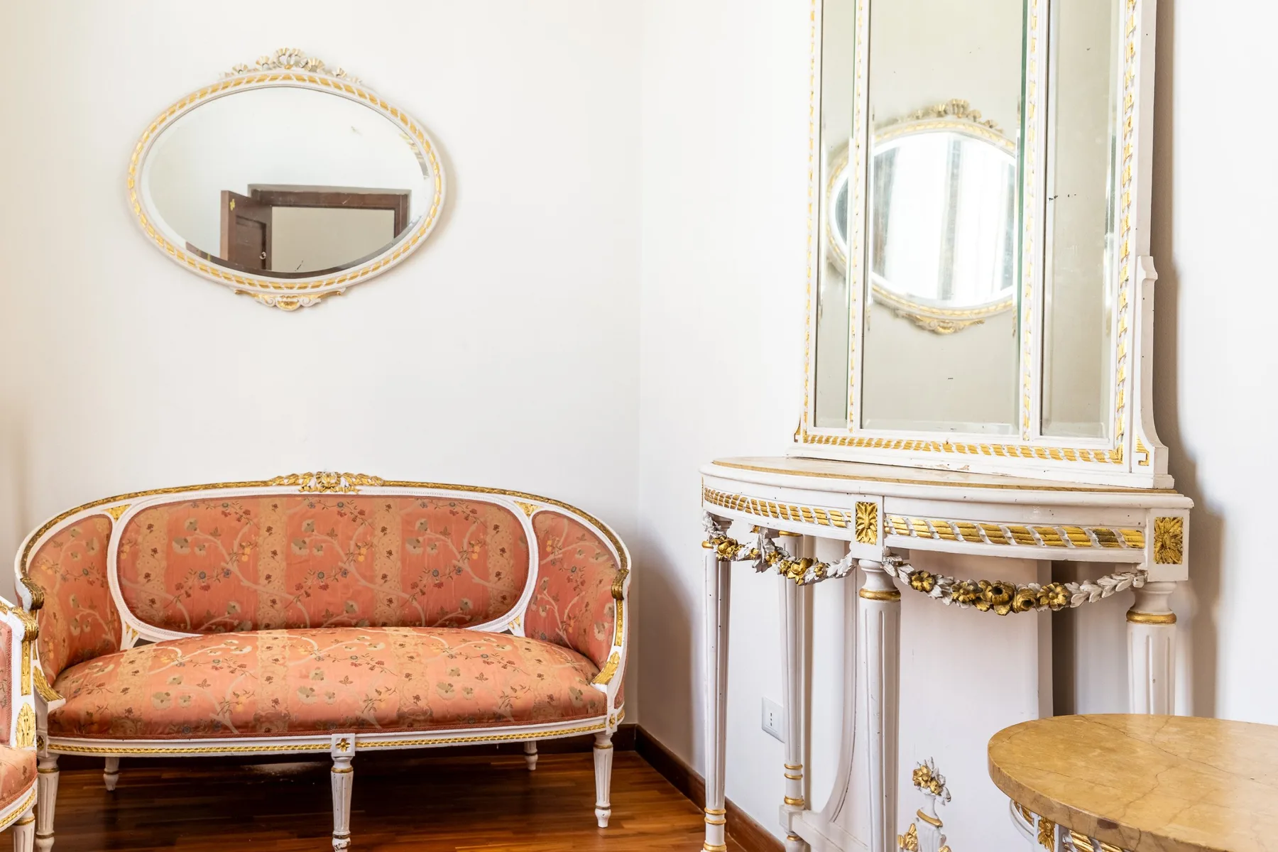 Una zona de estar decorativa cuenta con un asiento tapizado junto a una consola ornamentada con espejo.