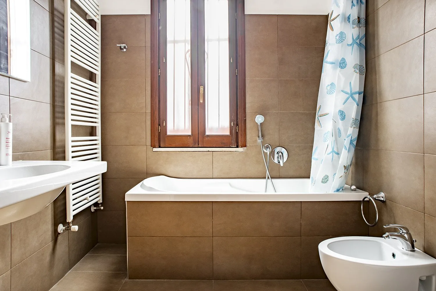 Un baño alicatado con una bañera bajo una ventana y un lavabo.