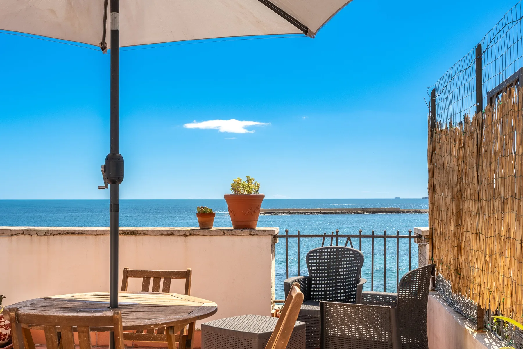 Una terraza junto al mar con asientos al aire libre y plantas en macetas frente al agua.