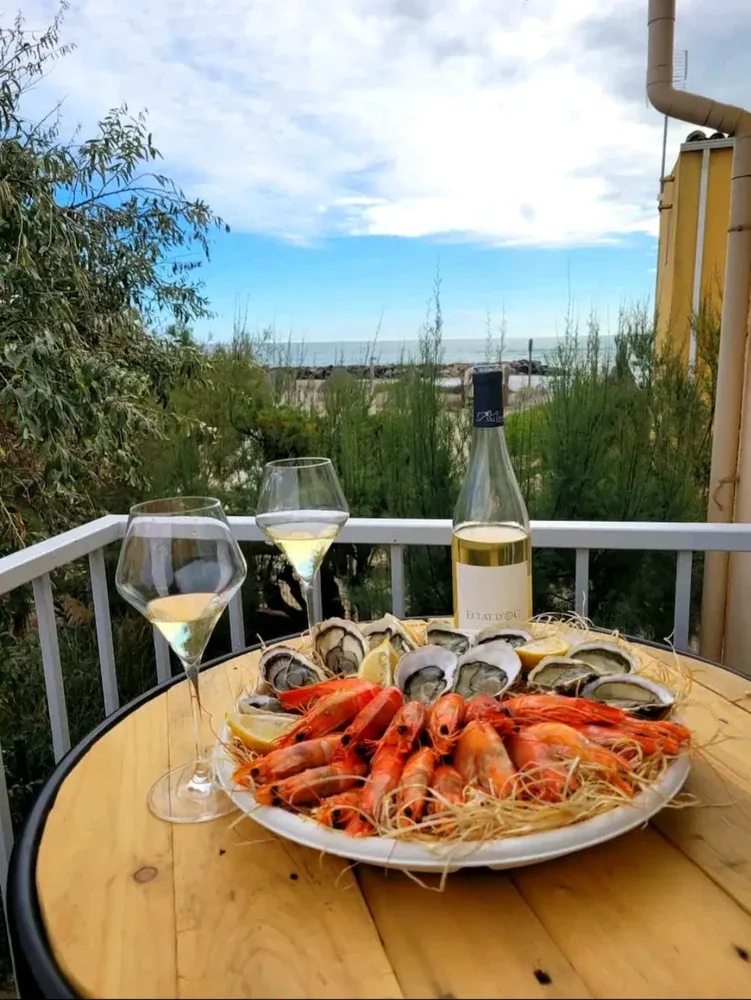 Una bandeja de mariscos y vino están sobre una mesa redonda al aire libre frente al mar.