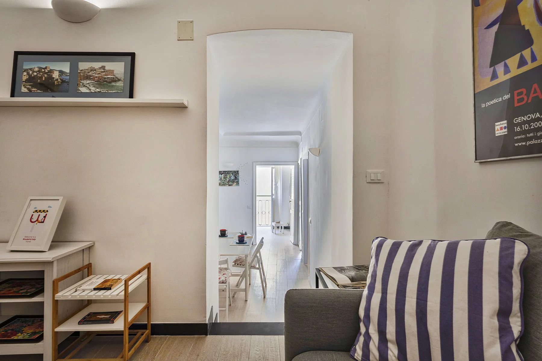 Una sala de estar con un cojín a rayas y una puerta abierta hacia un pasillo luminoso.
