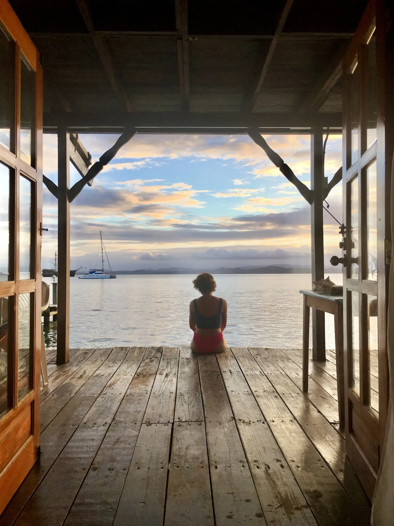A woman sits on a wooden deck overlooking the ocean.