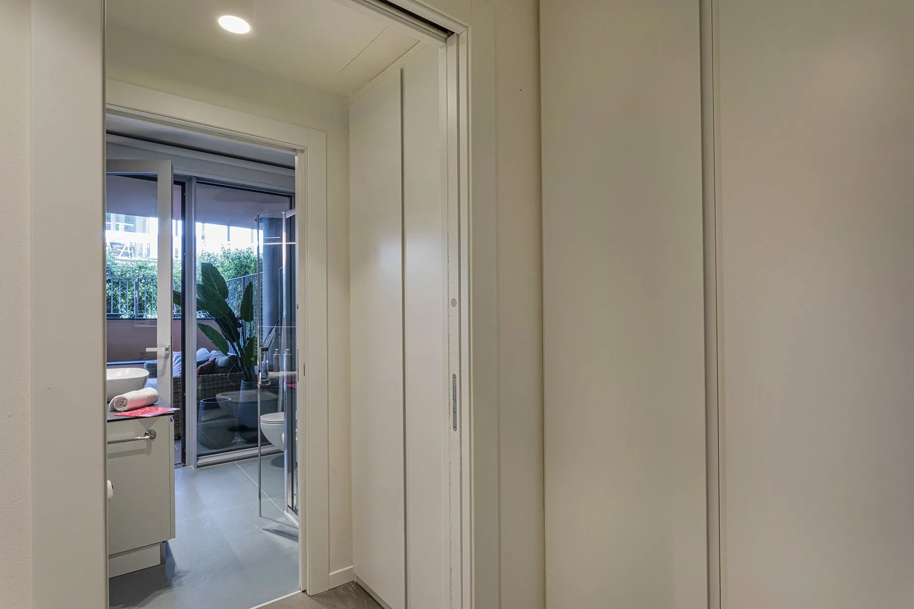 A hallway opens onto a bright room with glass doors and plants.