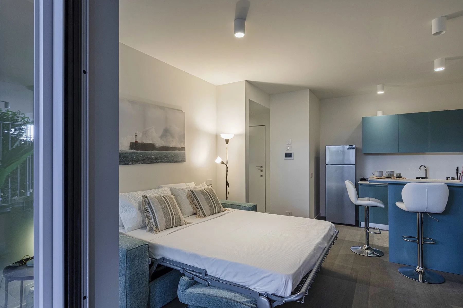 A bedroom with a neatly made bed beside a compact kitchen.
