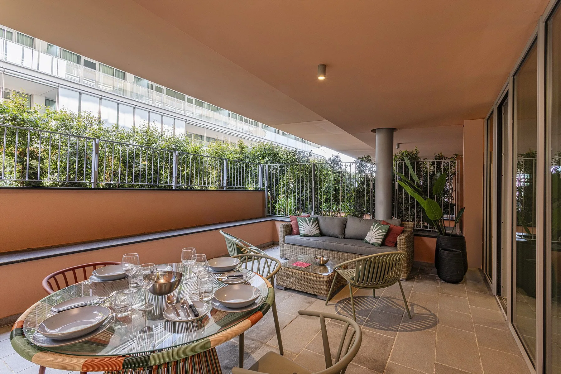 A covered balcony seating area has a dining table and potted plants.