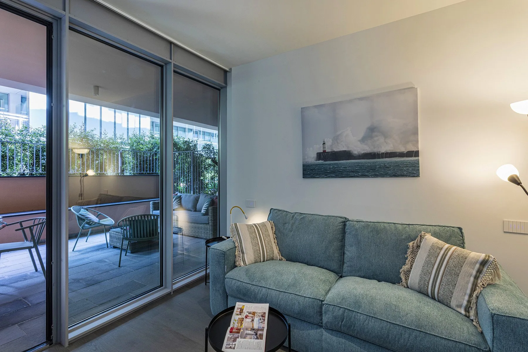 A living room with blue seating beside large glass doors opening onto a balcony.