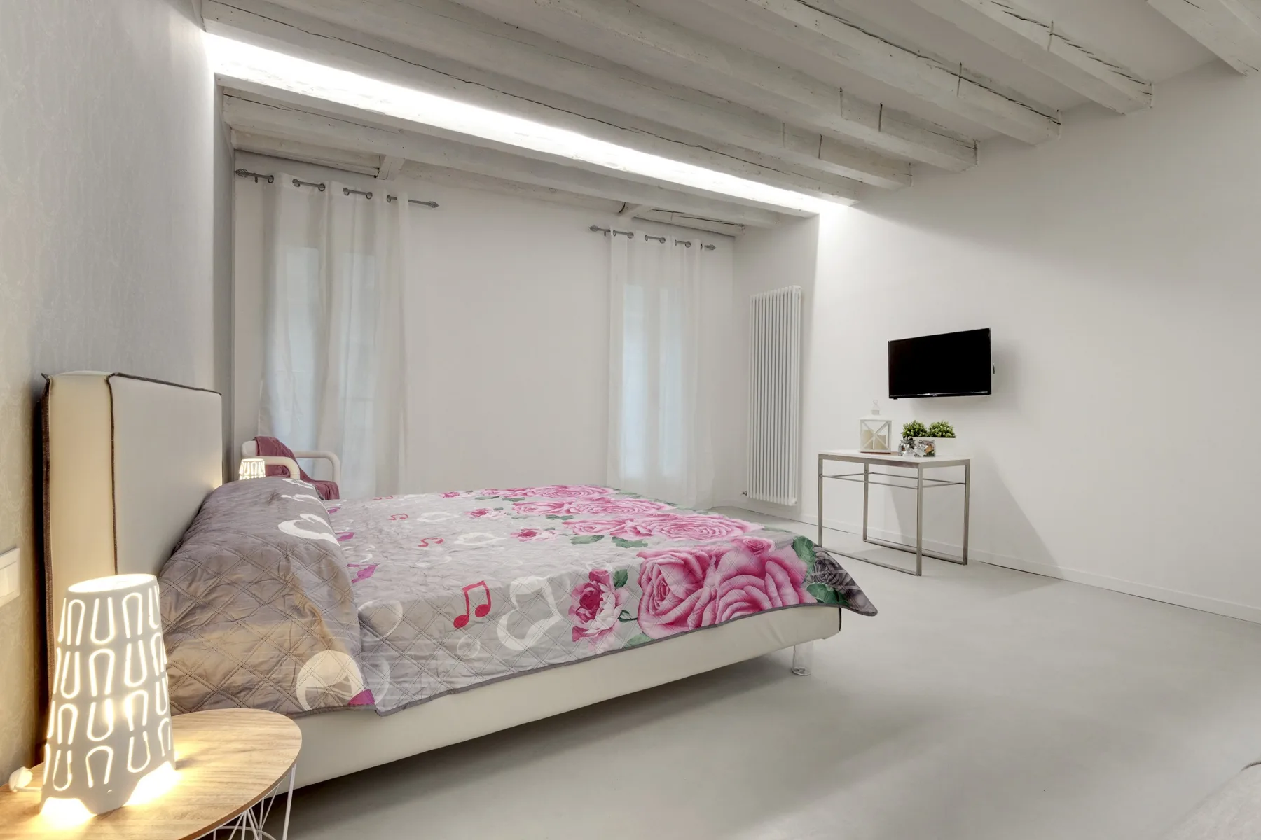 A bedroom with a bed, sheer curtains, and a wall-mounted television.