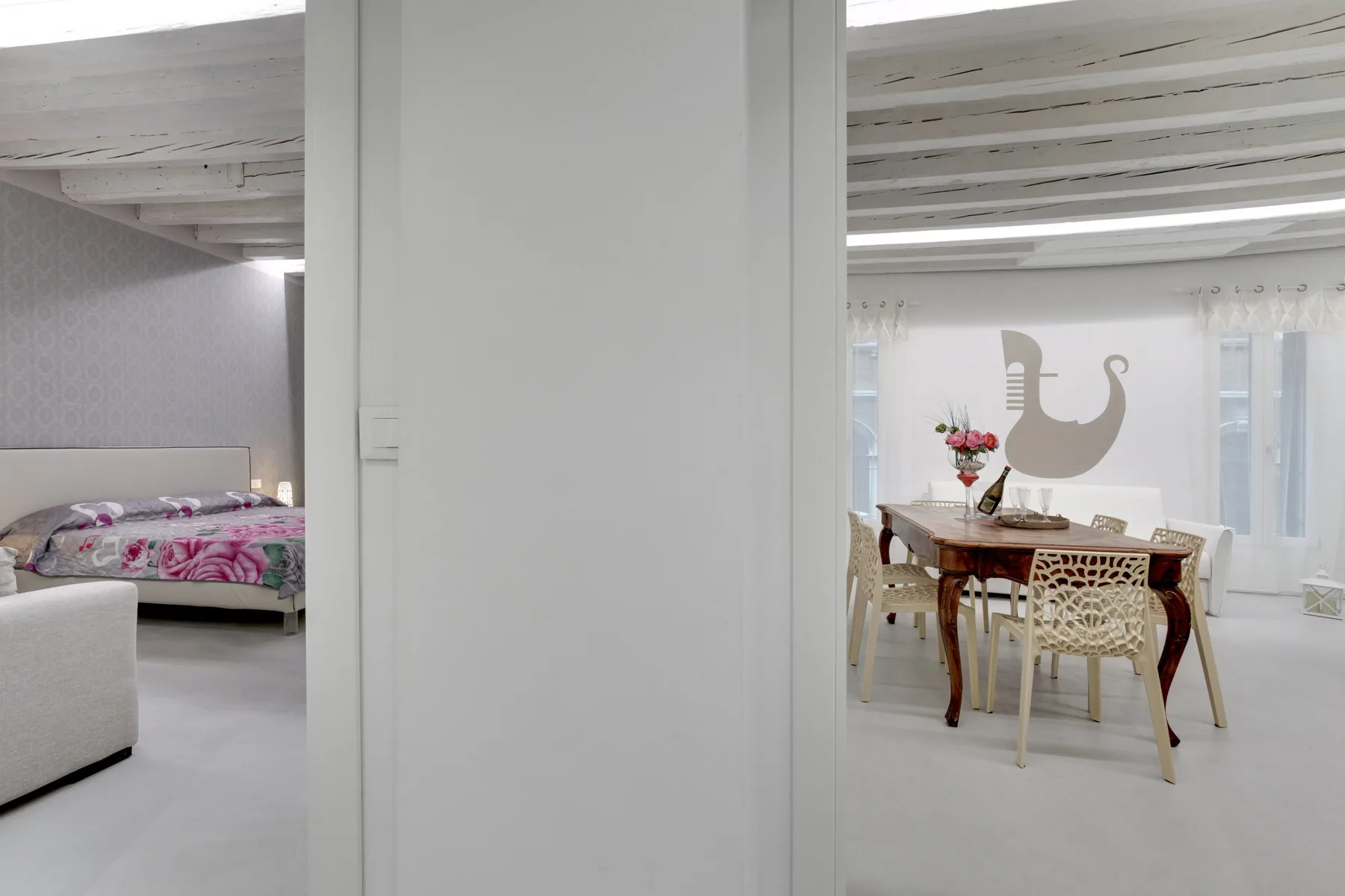 A white interior shows a dining table beside a bedroom.