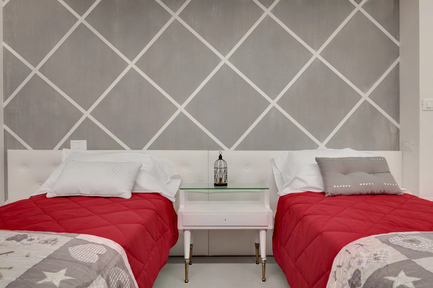 A bedroom with two beds covered in red bedding and a small table between them.